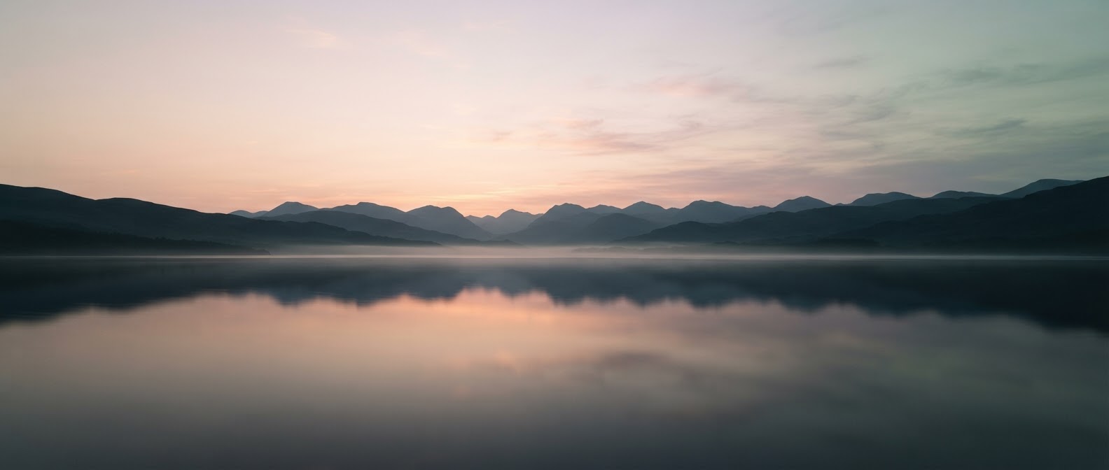 A wide calm lake at dawn with distant layered hills