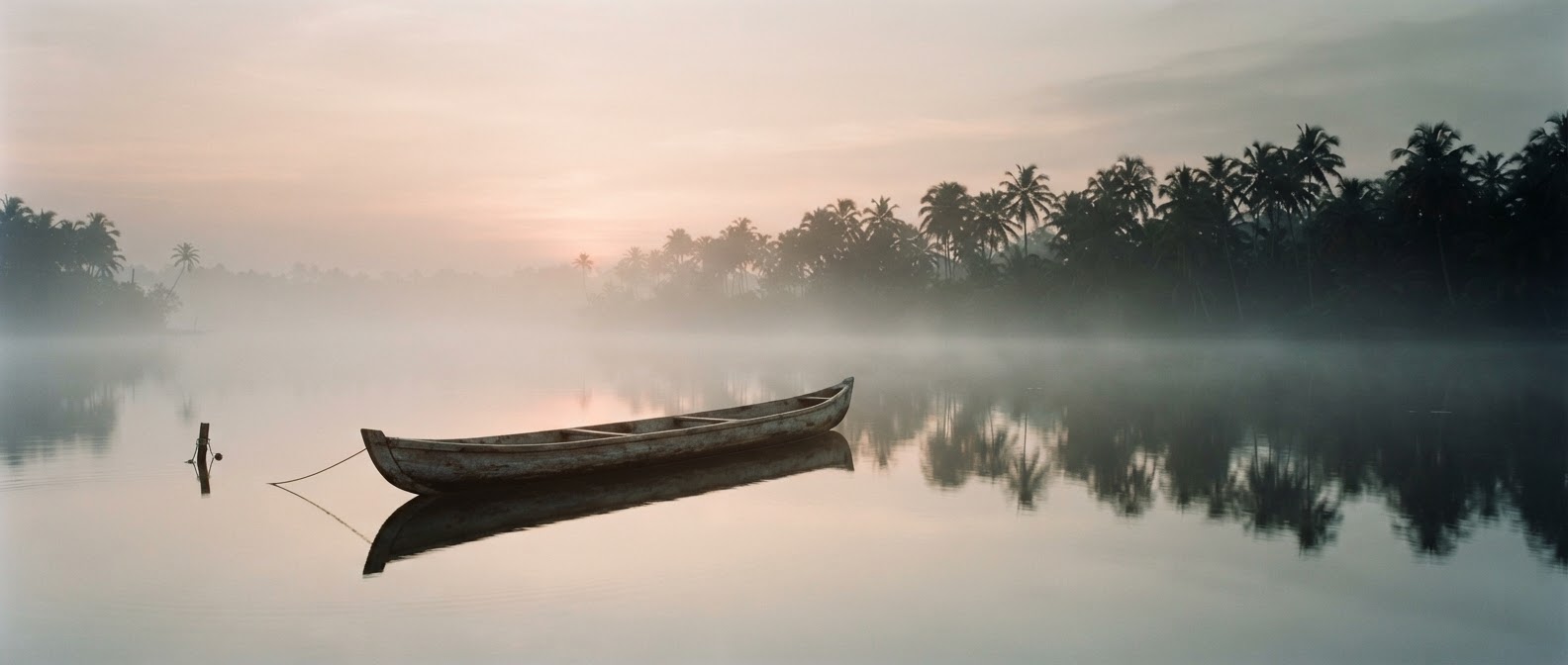 A wooden canoe on a still misty lake at first light